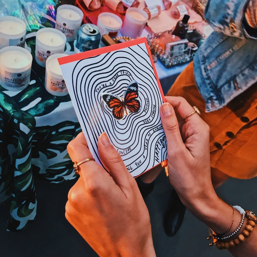 Woman's Hands Holding a card with a bright butterfly that is popping off the card at a farmers market